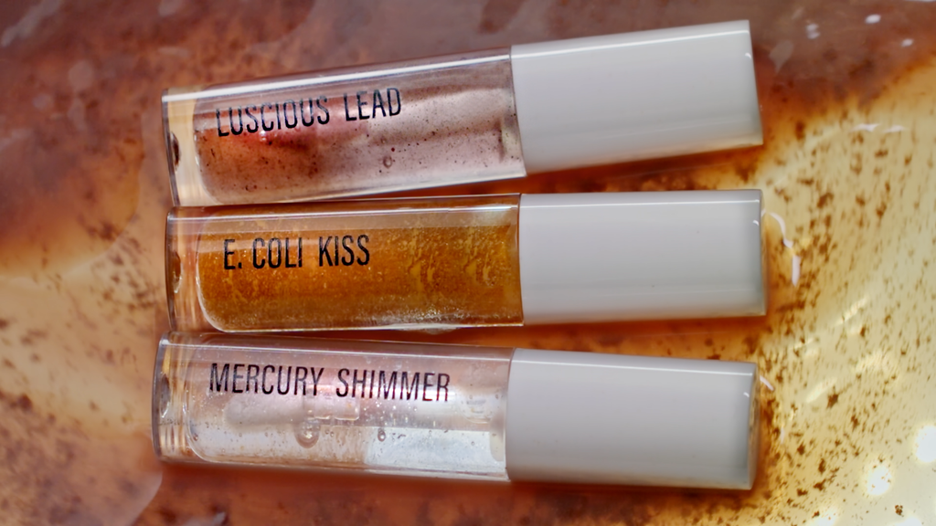3 lipglosses. The top lipgloss reads "Luscious Lead", the Center lipgloss reads "E.Coli Kiss", the bottom lipgloss reads "Mercury Shimmer"