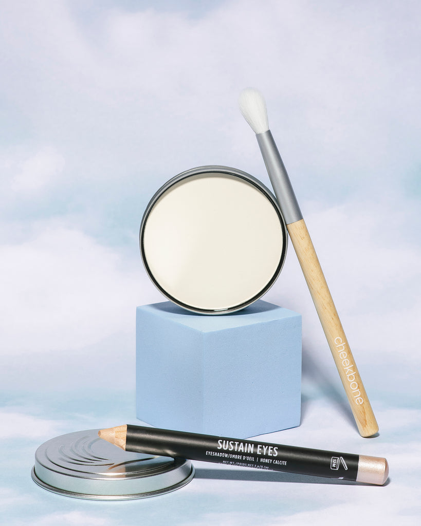  A small tapered blending eye shadow brush, Mattifying Moon Dust, Sustain Eyeshadow pencil on a blue sky background.